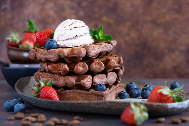 Chocolate Belgian waffles with fresh berries and coffee ice cream on a ceramic plate on brown table