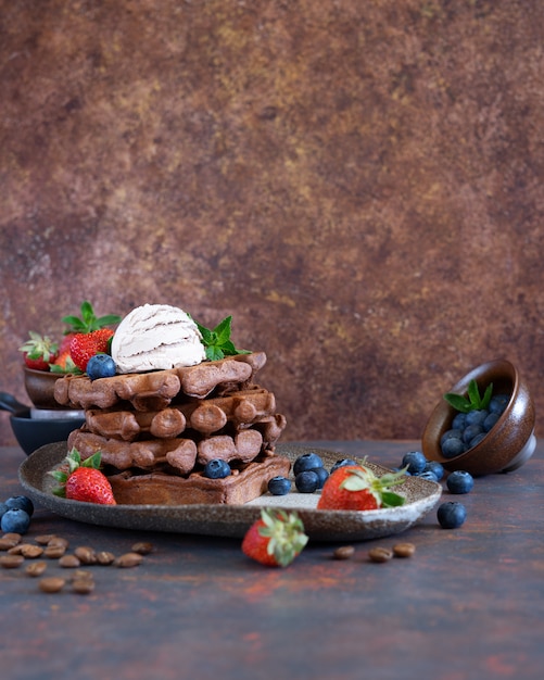 Chocolate Belgian waffles with fresh berries and coffee ice cream on a ceramic plate on brown table