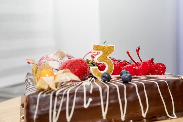 Chocolate birthday cake with berries and number three golden candles on white background copy spaceg