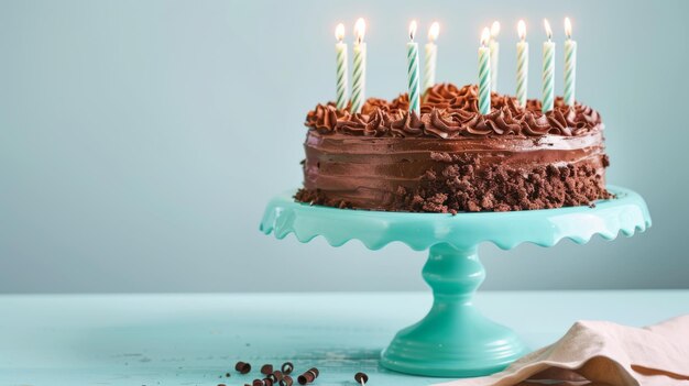 A chocolate birthday cake with lit candles on a turquoise cake stand