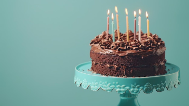 A chocolate birthday cake with lit candles on a turquoise cake stand