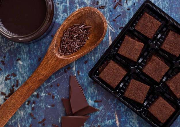 Chocolate biscuit shortcake dessert on blue board with jar of liquid chocolate and wooden spoon