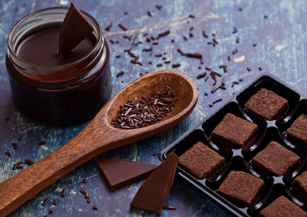 Chocolate biscuit shortcake dessert on blue board with jar of liquid chocolate and wooden spoon