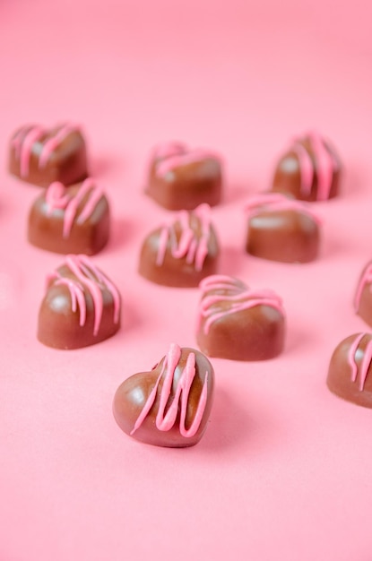 Chocolate bonbons in the shape of hearts with pink icing Pink plain background