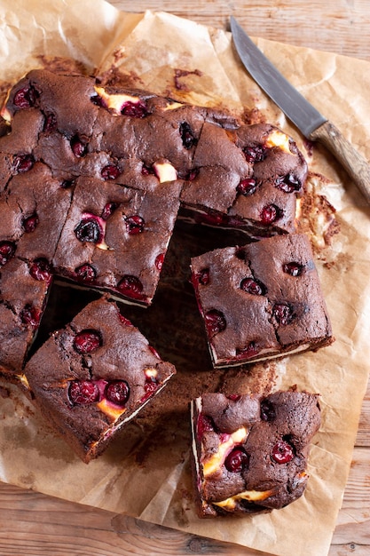 Chocolate brownie with cherries and cheese layer Many pieces of chocolate dessert on a wooden board