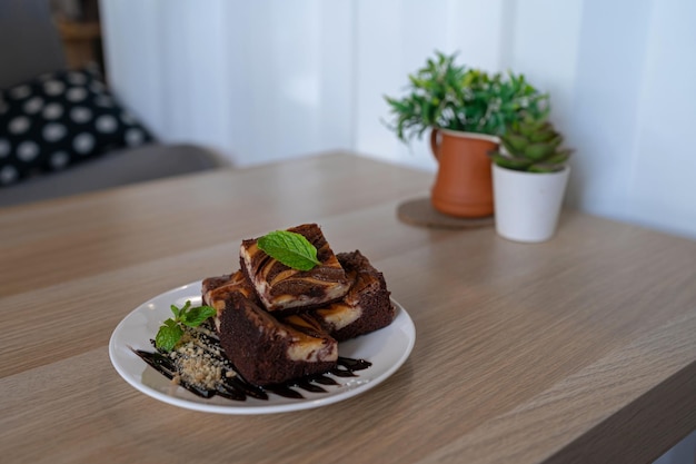 Chocolate brownie with sauce and nuts decorated with mint leaf on cozy wooden table