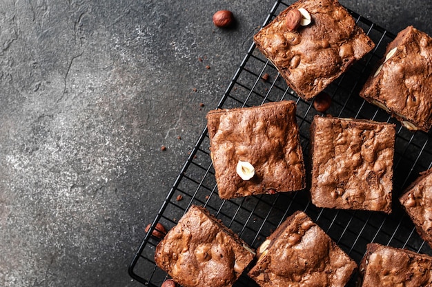 Chocolate brownies with nuts on baking rack on dark background top view text space