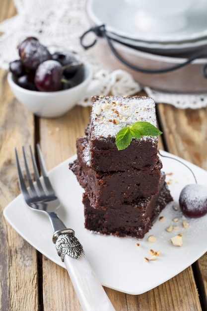 Chocolate brownies with powdered sugar and cherries on a dark wooden