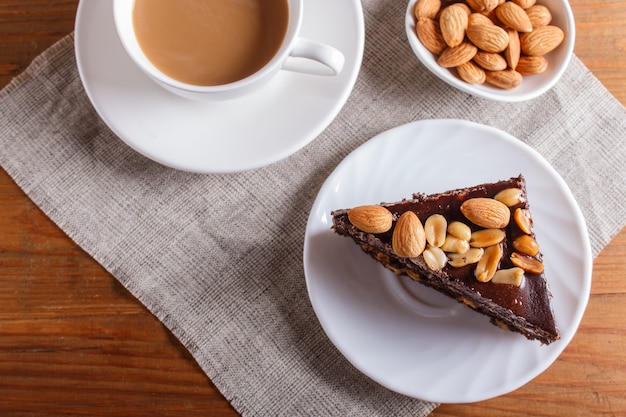 Chocolate cake with caramel, peanuts and almonds on a brown wooden background. 