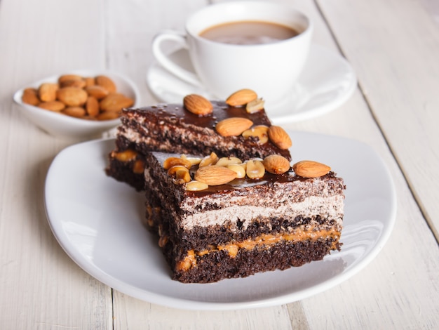 Chocolate cake with caramel, peanuts and almonds on a white wooden background. 