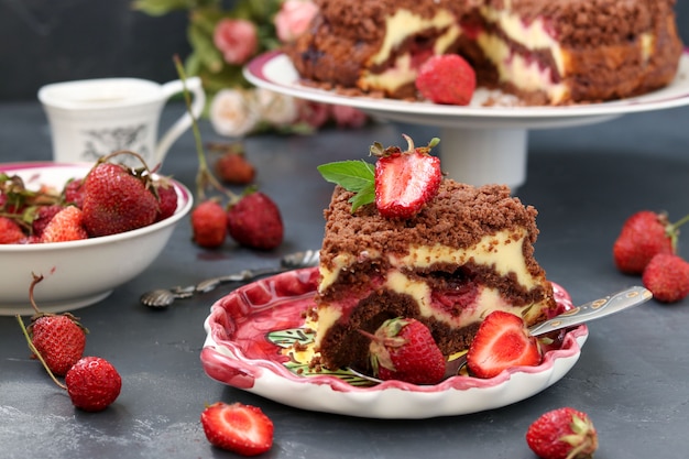 Chocolate cake with cottage cheese with strawberries is located on a dark , a piece of cake is located in the foreground on a plate