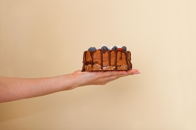 Chocolate cake on woman hand small pie with berries Ladys Hand holding tart over beige background