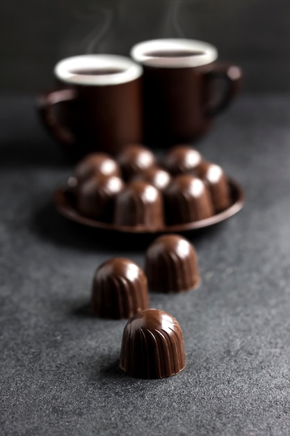 Chocolate candies on a plate and two cups of coffee on black surface