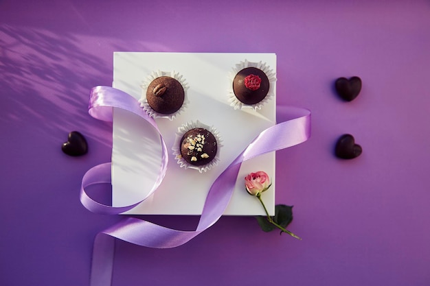 Chocolate candies with shadows Holidays and celebration concept Purple ribbon Purple color pattern background top view