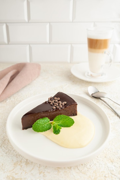 Chocolate cheesecake with butter cream. Decorated with mint. On a flat white plate. Light background.