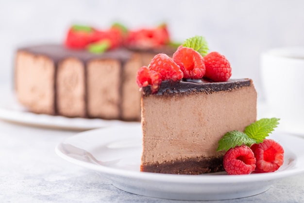 Chocolate cheesecake with fresh raspberries and mint leaves. A piece of cake is cut and served on a plate. Homemade dessert. Close-up.