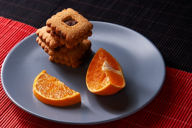 Chocolate chip cookies and piece of orange on plate and on red and black surface with place for text selective focus with copyspace