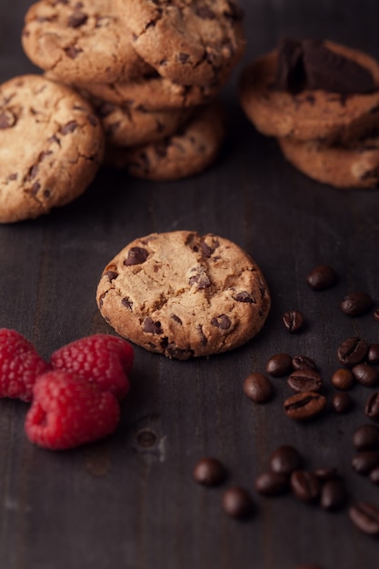 Chocolate chips cookies with red raspberries and coffee beans on dark old wooden table. Fresh out of the oven.