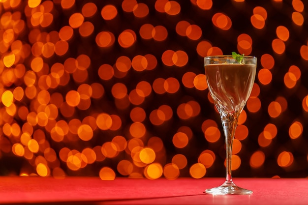 Chocolate cocktail with nuts and mint in a glass against a surface of blurry lights