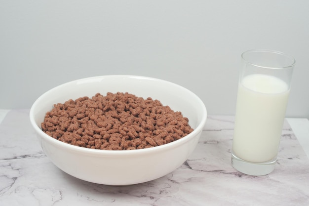 Chocolate corn flakes in a bowl and glass of milk on table