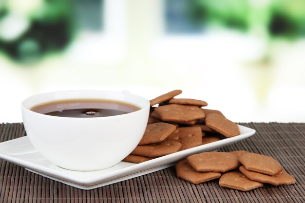 Chocolate crackers with cup of tea on bamboo mat on bright background