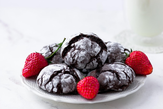 Chocolate cracks cookies on a white marble table Delicious cookies a cup of milk and strawberries