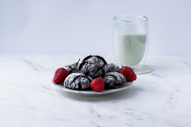 Chocolate cracks cookies on a white marble table Delicious cookies a cup of milk and strawberries