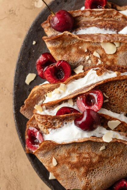 Chocolate crepes with cherry and whipped cream and almond petals on brown textured background