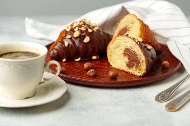 Chocolate croissant on clay plate with cup of coffee on table