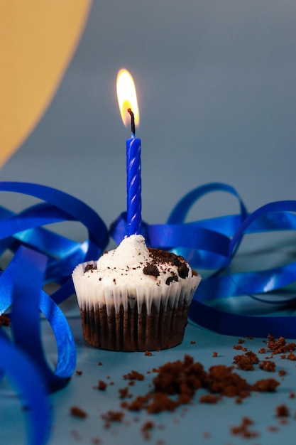 chocolate cupcake with a blue candle, blue background and blue ribbon