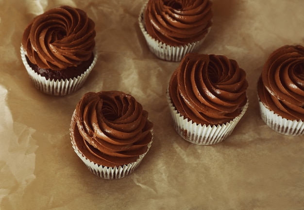 Chocolate cupcakes on baker paper over wooden background