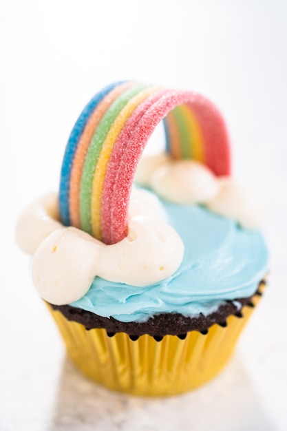 Chocolate cupcakes decorated with blue buttercream frosting and rainbow for unicorn theme birthday party.