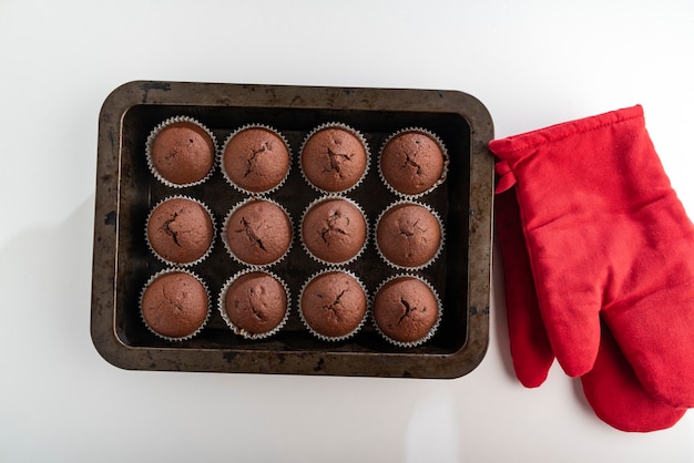 Chocolate cupcakes and red potholders on white background Top view Homemade coffee muffin Sweet pastries