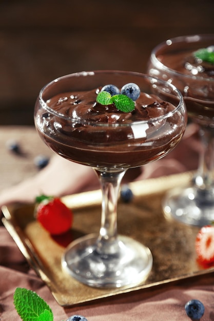 Chocolate dessert in glasses and fresh berries on color wooden background