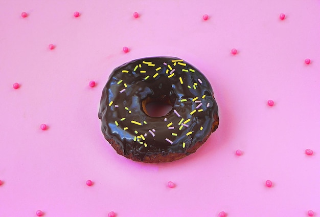 Photo a chocolate donut with sprinkles on a pink background