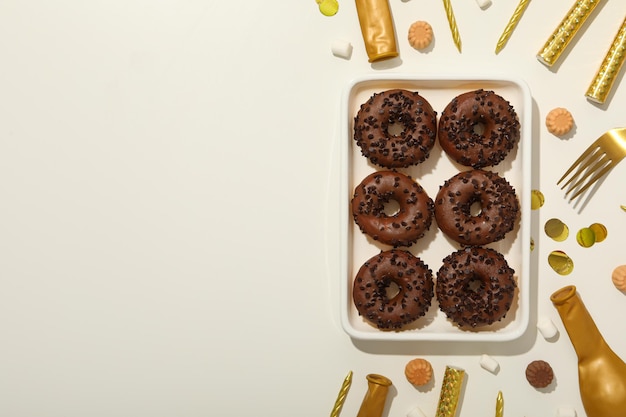 Chocolate donuts on plate and party supplies on white background space for text