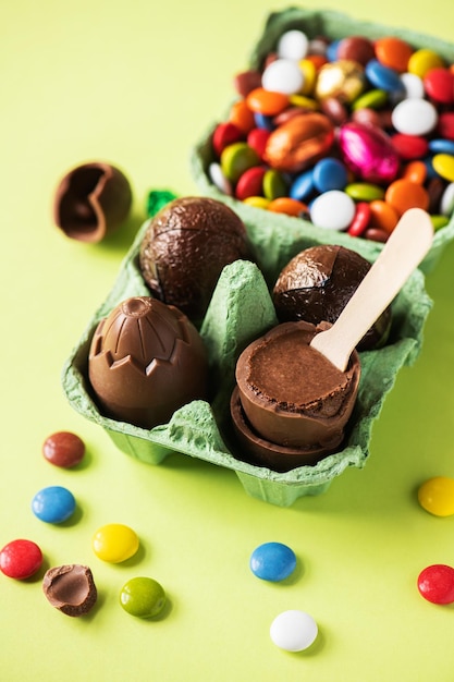 Chocolate Easter eggs with cream filling and colorful candies on a green background Top view