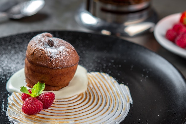 Chocolate fondant cake with vanilla cream, raspberry and mint on a black plate