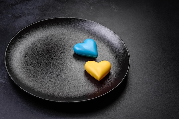 Chocolate hearts in the colors of the Ukrainian flag on a black ceramic plate