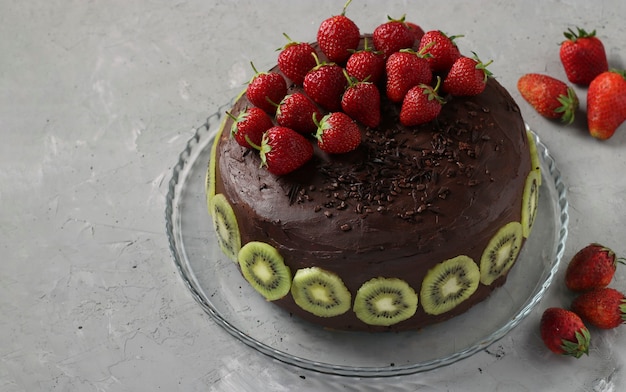 Chocolate homemade cake decorated strawberries and kiwi located on gray concrete background, horizontal format, Closeup, Copy space