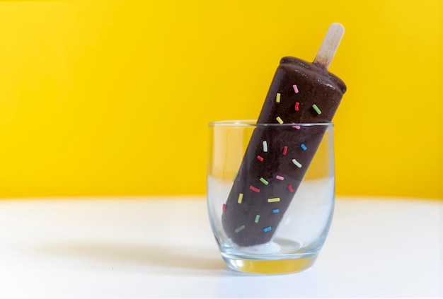 Chocolate ice cream covered in colored nuggets in a glass about to melt Yellow background