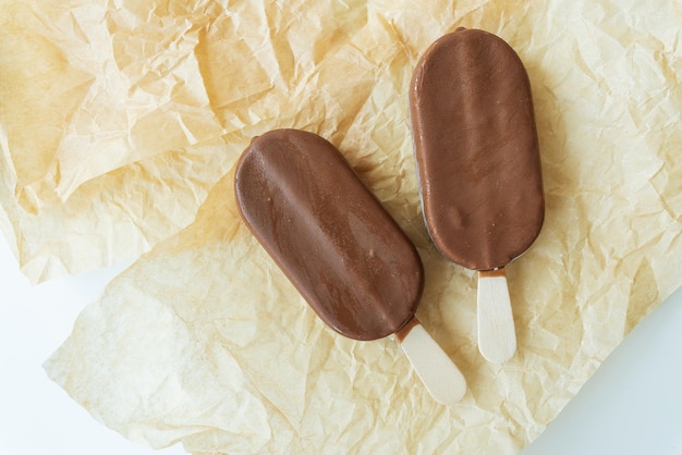 Chocolate ice cream on a stick lies on parchment covered with chocolate warm cold delicious ice cream Summer rest View from above