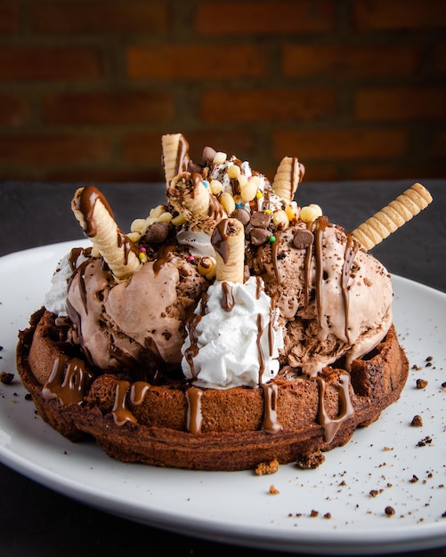 Chocolate ice cream and waffles, with cream and chocolate syrup, black background, brick wall