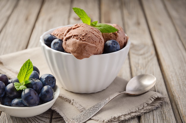 Chocolate ice cream with blueberries in white bowl on rustic wooden background