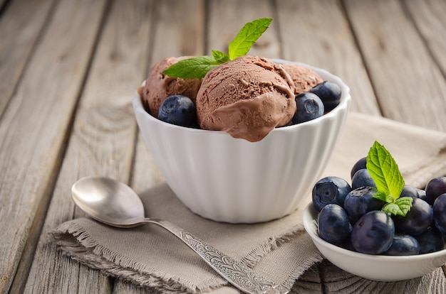 Chocolate ice cream with blueberries in white bowl on rustic wooden table.