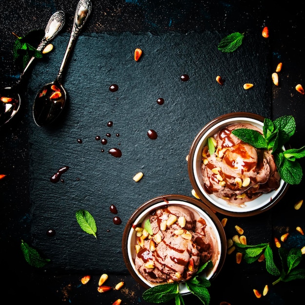 Chocolate ice cream with topping and fried pine nuts decorated with mint leaves dark background top view