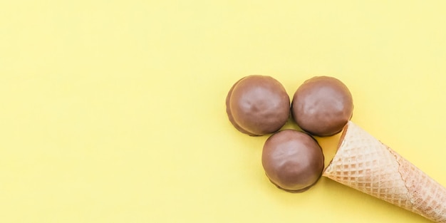 Chocolate ice cream with a waffle cone of three chocolate candy biscuits on a yellow background