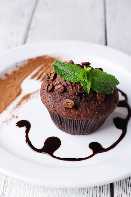 Chocolate muffin with chocolate sauce on plate on wooden background