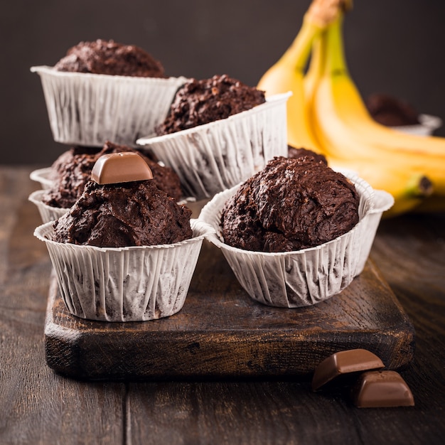 Chocolate muffins with banana in white paper cups on dark wooden surface. Party food concept