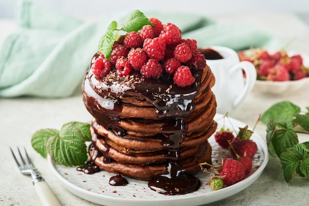 Chocolate Pancakes Pancakes with fresh raspberry with chocolate glaze or toppings in gray bowl on light gray table background Homemade classic american pancakes Page for magazine concept